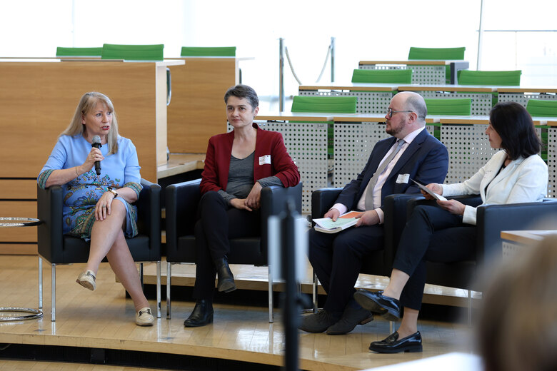 Staatsministerin Petra Köpping diskutiert mit drei weiteren Gesprächspartnern. Alle vier sitzen auf Stühlen vor der Regierungsbank im Plenarsaal des Sächsischen Landtags.